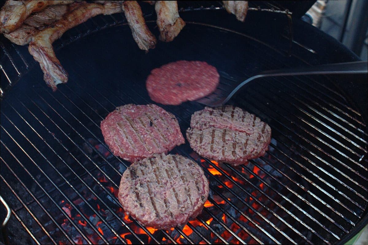 A burger being placed onto a hot cooking surface with tongs