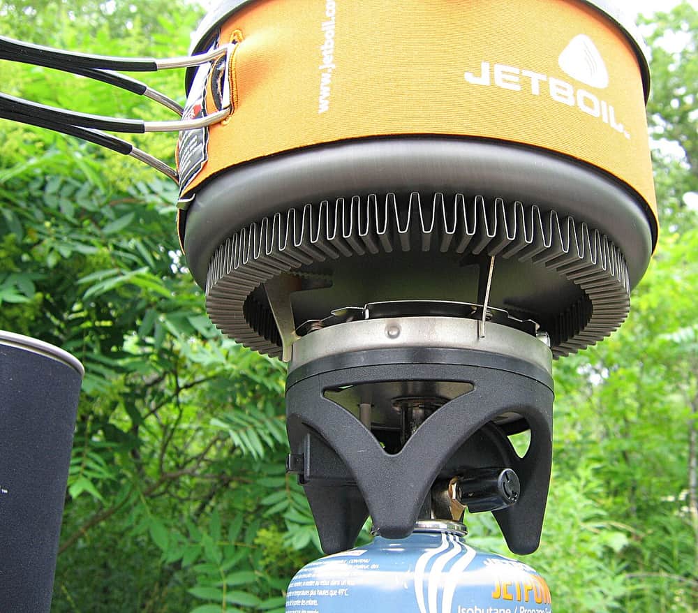 A portable camping stove burning under a cooking pot